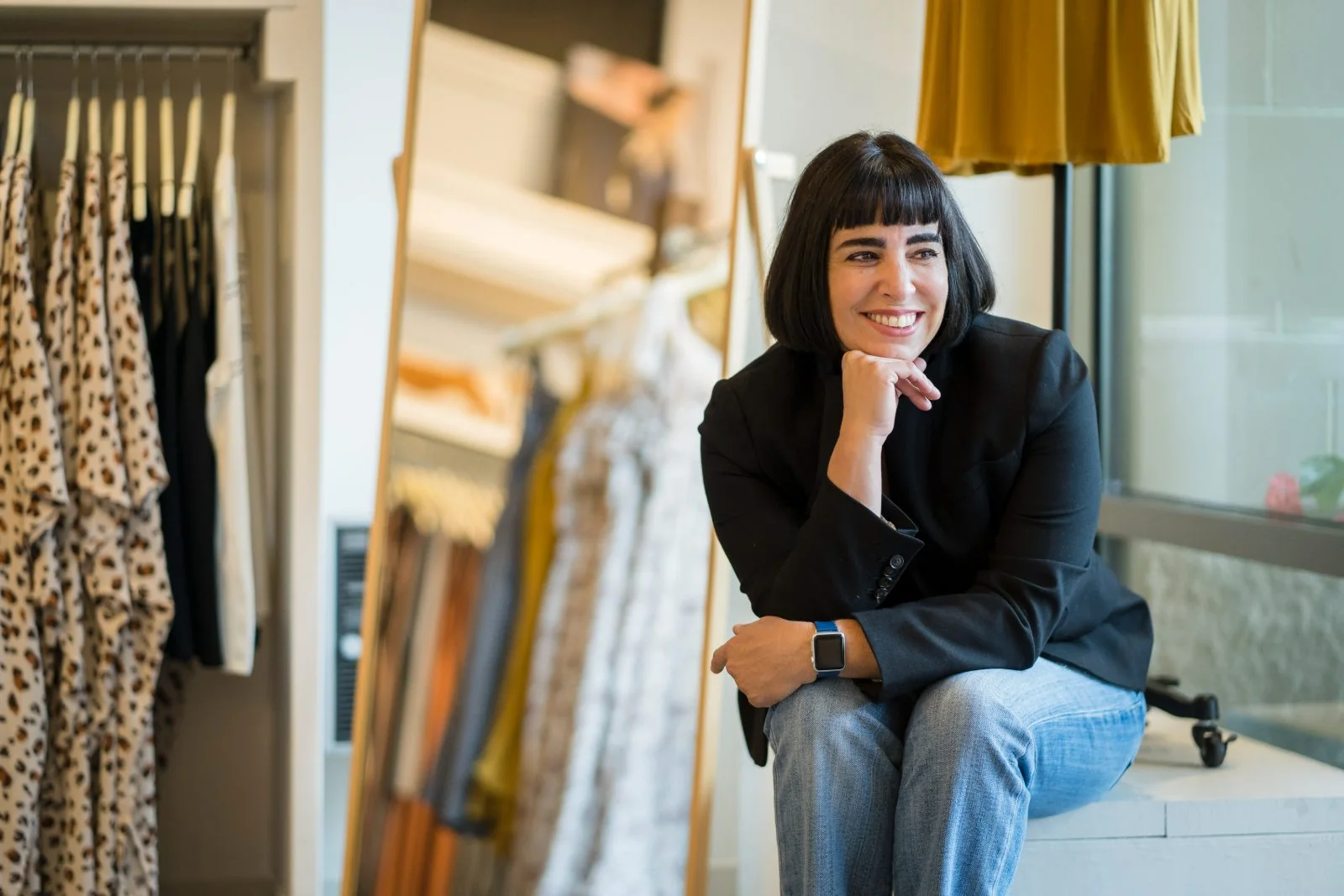 Rachel Williamson seated in a boutique, chin resting on her hand, smiling toward the sales floor
